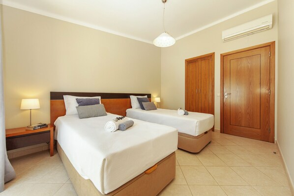 Una habitación de hotel con dos camas, una mesita de noche, una lámpara y un armario.