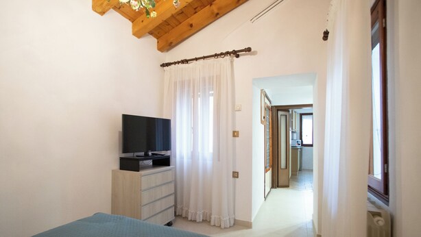 A bedroom with a bed, a TV on a dresser, and a hallway leading to a bathroom. - Dimora Alba di Mare -apeliving- Pellestrina Ve (Venezia)