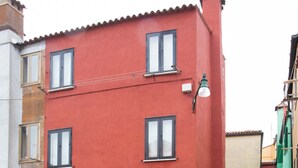 A red building with multiple windows and a door, surrounded by a cobblestone courtyard. - Dimora Alba di Mare -apeliving- Pellestrina Ve (Venezia)