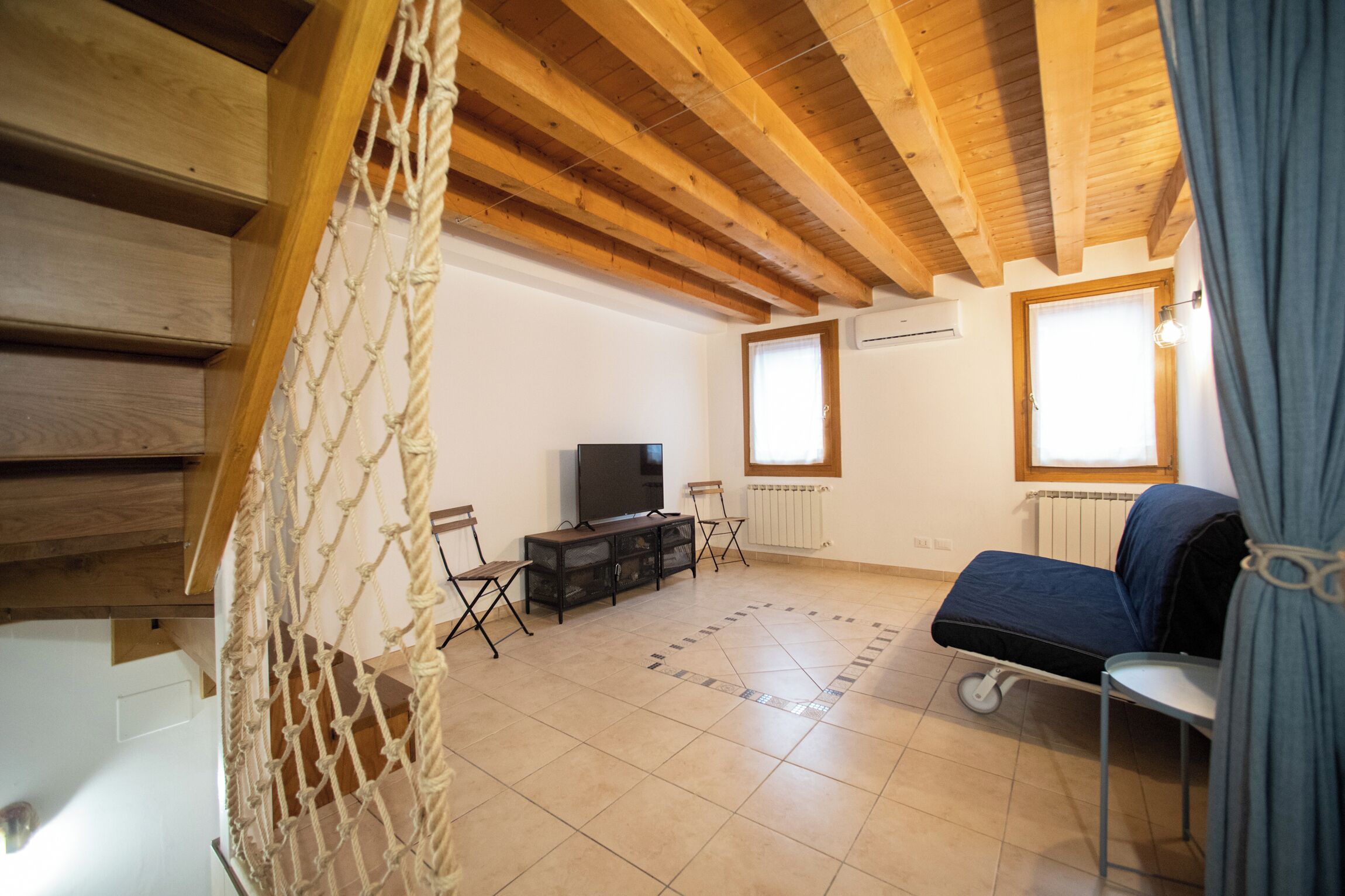 Un accogliente soggiorno con soffitto in legno, una televisione su supporto nero, un divano blu e un tavolino.
