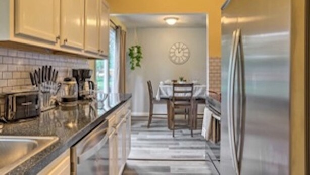 A modern kitchen with stainless steel appliances, a dining area with a table and chairs, and a clock on the wall. - Cozy Home with a Huge Backyard! (Parma Heights)