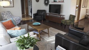 Ein Wohnzimmer mit einer Couch, Sesseln, einem Couchtisch, einem Fernseher und einem Bücherregal.