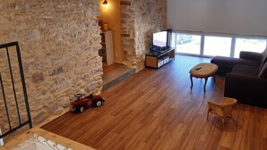 Un salon avec un mur en pierre, un plancher en bois, un canapé, un meuble pour la télévision et une voiture jouet.