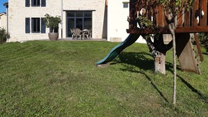 Une maison à deux étages avec une façade en pierre, une terrasse en bois et un toboggan.