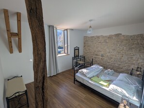 Ein Schlafzimmer mit Steinwand, einem Bett, Holzboden, einem Fenster mit Vorhängen und einem Sessel.