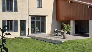 Une maison moderne avec une façade en pierre, une terrasse en bois et un patio aménagé avec du mobilier d’extérieur.