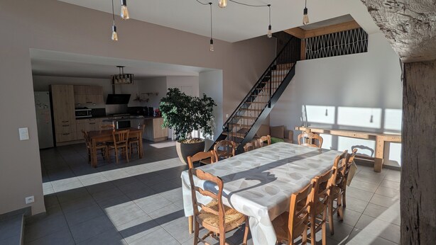 Un vaste espace de vie comprenant une table à manger, des chaises, une grande plante en pot et un escalier.