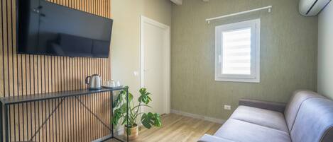 A modern living room with a wooden panel wall, a flat-screen TV, a sofa, a coffee table, and a potted plant.