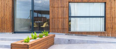 A modern building with wooden paneling, large glass windows, and a built-in planter with green plants.