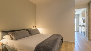 Een moderne slaapkamer met een groot bed, een nachtkastje en uitzicht op de woonkamer.