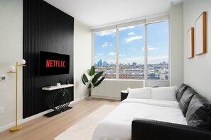 A modern living room with a large window, a black entertainment unit, and a bed.