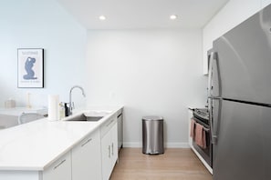 A modern kitchen with white cabinetry, a stainless steel refrigerator, a sink, and a trash can. - Exclusive 1BR Apt | Midtown NYC Skyline View (Hoboken)