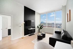 A modern living room with a black entertainment unit, a large window with a city view, a black sofa, and a white armchair.