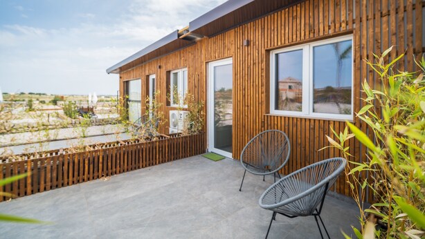 En moderne bygning med træfacade, store vinduer og en patio med to stole.