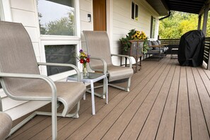 Une véranda couverte avec des chaises et une table en métal, un barbecue et un vase à fleurs.