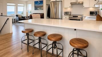 A modern kitchen with a large island, bar stools, stainless steel appliances, and a view of the ocean.