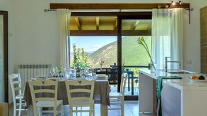 A dining area with a table set for four, a kitchen with a sink and countertop, and a view of a mountainous landscape. - Acquanera 6&2 by Marche Holiday Villas (Piobbico)