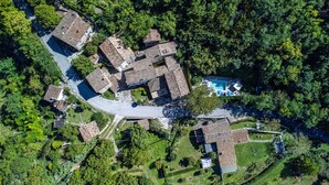 An aerial view of a residential area with multiple houses, a swimming pool, and a winding road. - Acquanera 6&2 by Marche Holiday Villas (Piobbico)