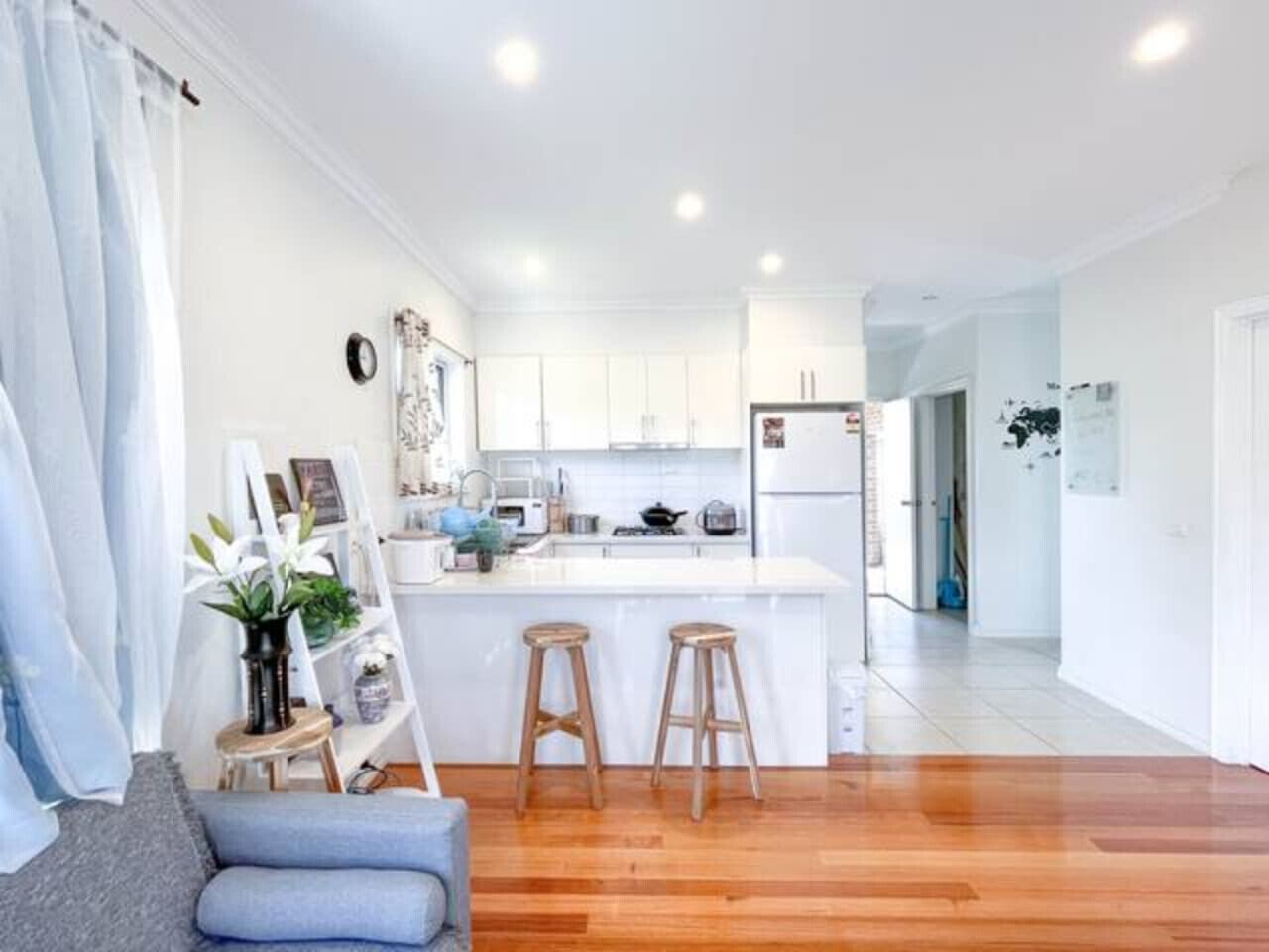 A modern kitchen with white cabinets, a central island with stools, and a dining area with a grey sofa.