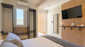 Et moderne hotelværelse med en stor seng, et tv ophængt på væggen og et vindue med rullegardiner.