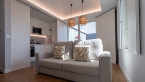 A modern living room with a sofa, two patterned cushions, a wooden coffee table, and a kitchen in the background.