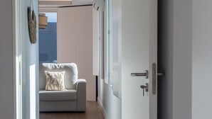 A narrow hallway with a grey sofa and a white door.