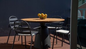 A round table with a wooden top and metal chairs, accompanied by a fruit bowl.
