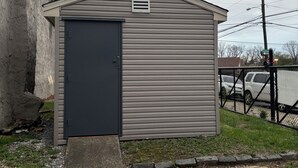 A small, single-story shed with a dark door and a vent on the roof.