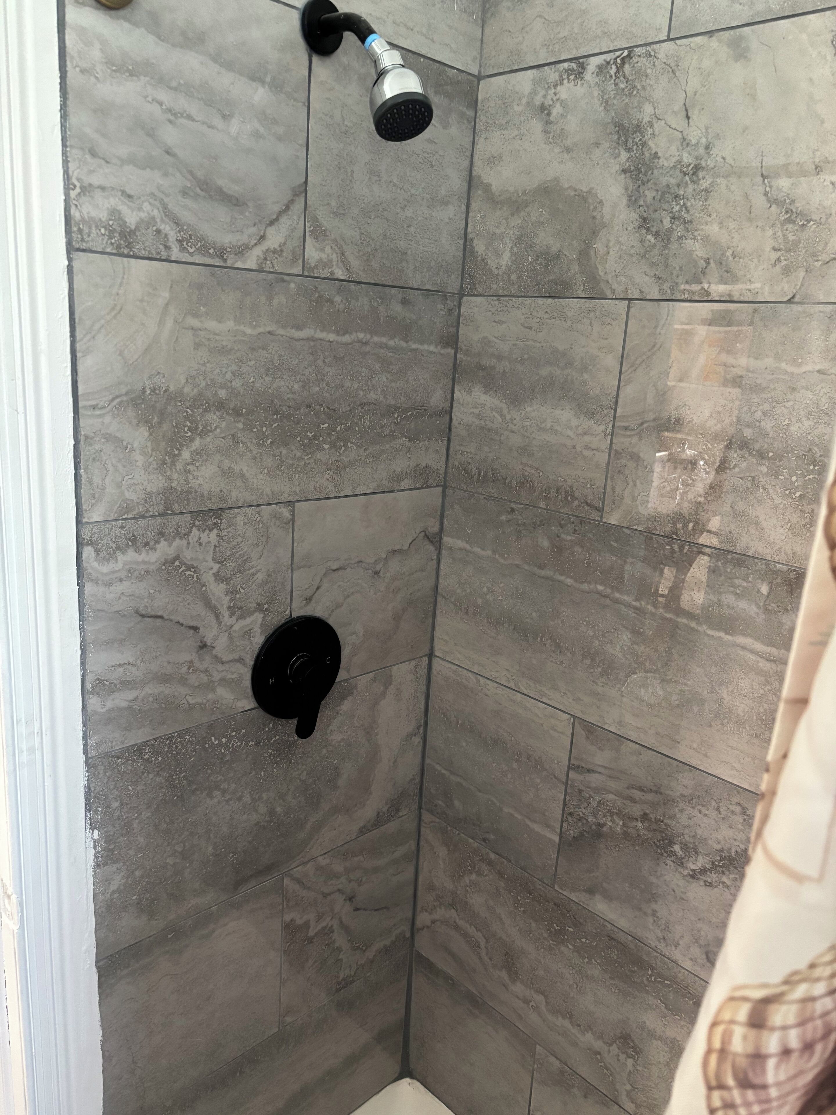 A shower area with grey tiles and a handheld showerhead.
