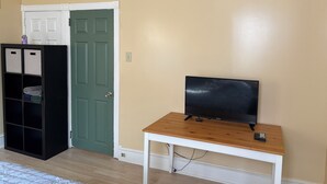 A room with a green door, a black wardrobe, a white bed, and a wooden table with a TV and remote controls.