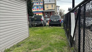 A fenced yard with two parked vehicles and a building with a colorful facade in the background.
