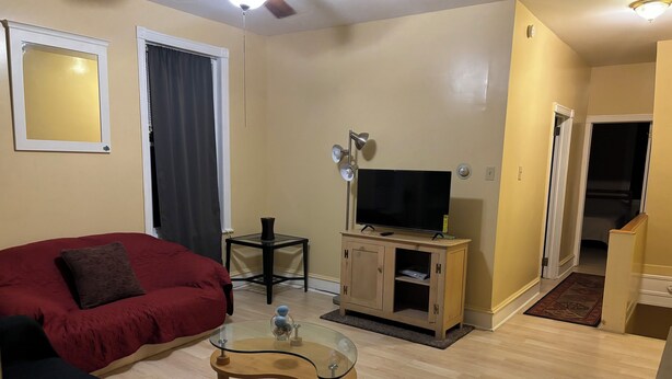 A living room with a red sofa, a glass coffee table, a TV on a wooden cabinet, and a ceiling fan.