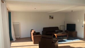 Una sala de estar con un sofá, dos sillones, una mesita de centro y un televisor.