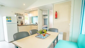 Een compacte keuken met een magnetron, koelkast en een klein eethoekje met een tafel en stoelen.