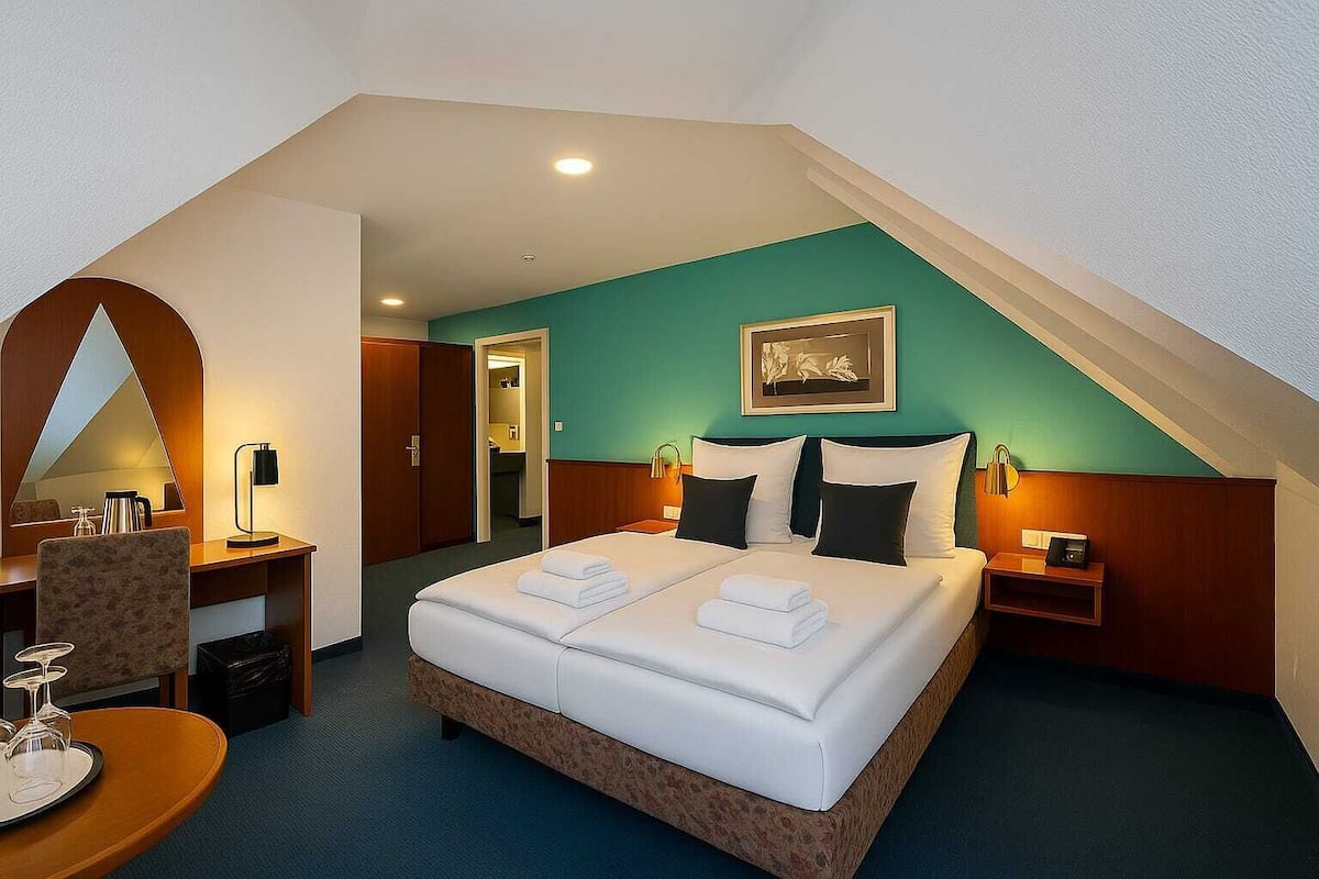 A hotel room with a large bed, a desk with a lamp, a chair, and a small table with a tray.