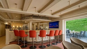 A bar area with a high bar and red bar stools, a kitchen area with a large island, and a seating area with wicker chairs. - AR Boutique Hotel Mannheim City (Mannheim)
