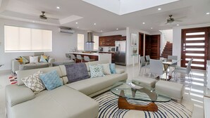 A modern living room with a sectional sofa, a glass coffee table, and a dining area with a glass table and chairs. - 4-Bedroom Oceanview Villa | Private Pool & Yard (San Juan del Sur)