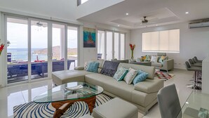 A spacious living room with a large glass coffee table, a beige sofa with patterned cushions, and a view of the ocean through floor-to-ceiling windows. - 4-Bedroom Oceanview Villa | Private Pool & Yard (San Juan del Sur)