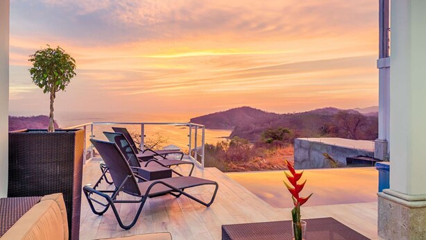 A terrace with lounge chairs and a potted plant, overlooking a body of water and hills during sunset. - 4-Bedroom Oceanview Villa | Private Pool & Yard (San Juan del Sur)