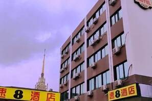 En hotellbyggnad med flera våningar och balkonger, ett markant torn i bakgrunden och en skylt som visar hotellets namn.
