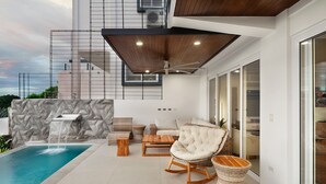 Un espace de vie extérieur moderne doté d’une piscine, de coins salon et d’une cascade décorative.
