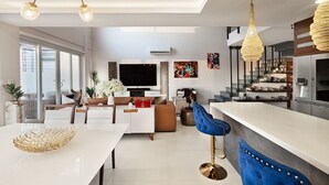 Un salon moderne doté d’un téléviseur à écran plat, d’un coin repas avec une table blanche et d’une cuisine  équipée d’un réfrigérateur en acier inoxydable.