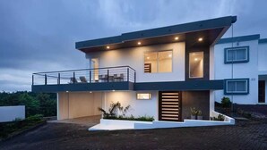 Une maison moderne à deux étages, dotée d’un balcon, de grandes fenêtres et d’une entrée bien éclairée.