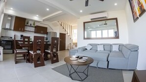 Un salon moderne avec un canapé gris, une table basse et un coin repas comprenant des chaises et une table. On y trouve également un ventilateur de plafond et un grand miroir accroché au mur.