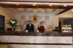 Ein Hotelrezeptionstresen mit Marmorplatte, zwei Rezeptionisten, einer Uhr und einem Schild für das Super 8 Motel.