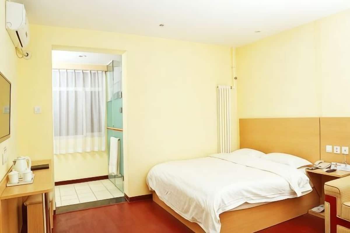 Habitación de hotel con cama, mesita de noche, espejo, ventana y zona de ducha.