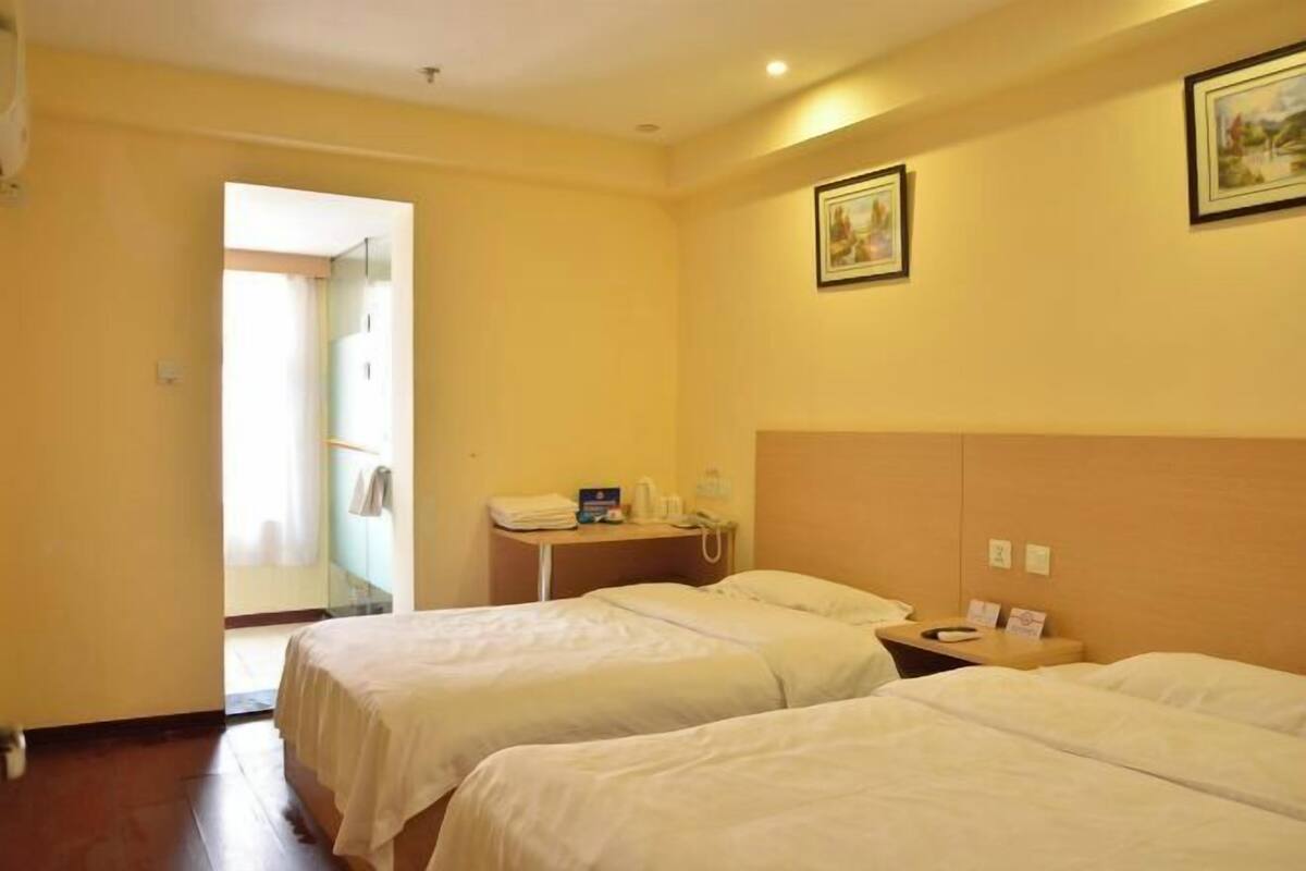 Una habitación de hotel con dos camas, una mesita de noche con un teléfono, una pequeña mesa con una lámpara y un cuadro en la pared.