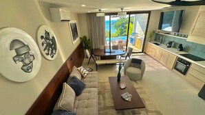 A modern living room with a sofa, coffee table, and dining area. There is a kitchen with a sink and stove, and a view of the ocean through large windows. - San Juan del Sur Villa | Infinity Pool Sunset View (San Juan del Sur)