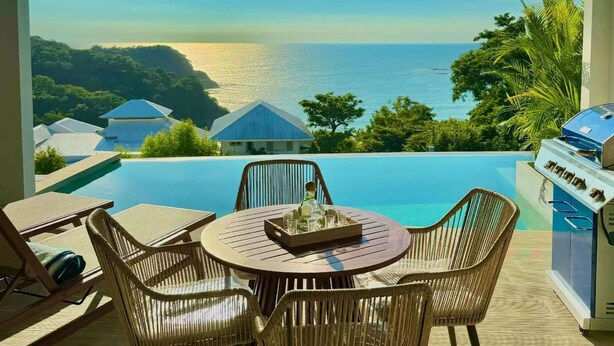 A balcony with a view of the sea, a round table with chairs, and a grill. - San Juan del Sur Villa | Infinity Pool Sunset View (San Juan del Sur)