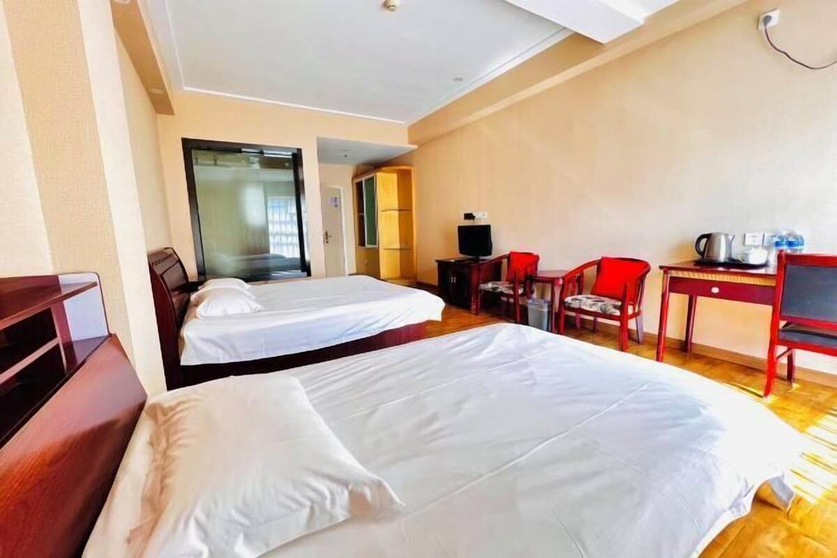 A hotel room with two beds, a desk with a chair, a television, and a small table with a kettle.